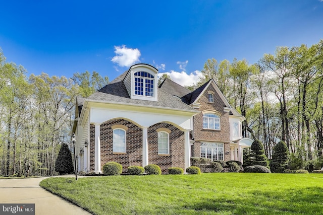 view of front of home with brick siding, roof with shingles, and a front yard