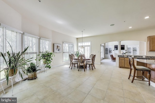 dining space featuring baseboards, arched walkways, light tile patterned floors, and ornate columns