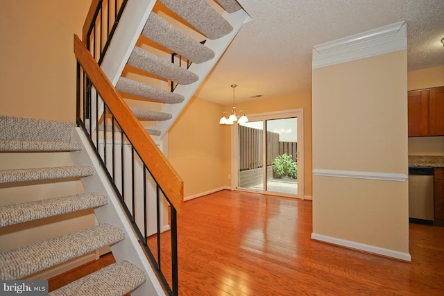 staircase with baseboards, a textured ceiling, wood finished floors, and a chandelier