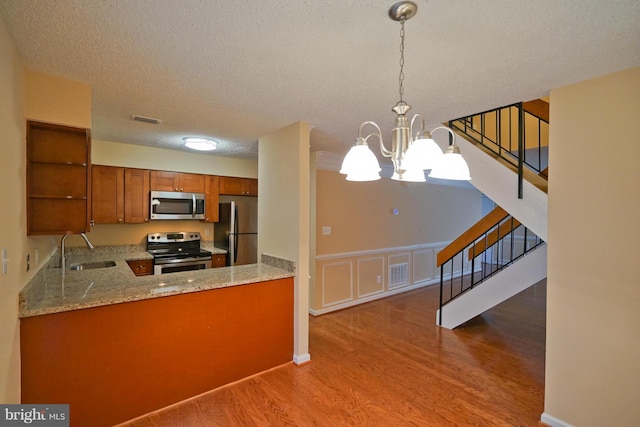 kitchen with brown cabinets, open shelves, appliances with stainless steel finishes, a sink, and visible vents