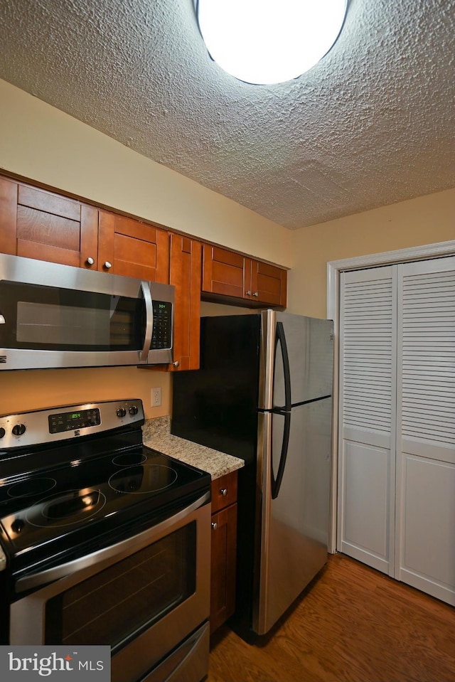 kitchen featuring appliances with stainless steel finishes, brown cabinetry, a textured ceiling, and wood finished floors