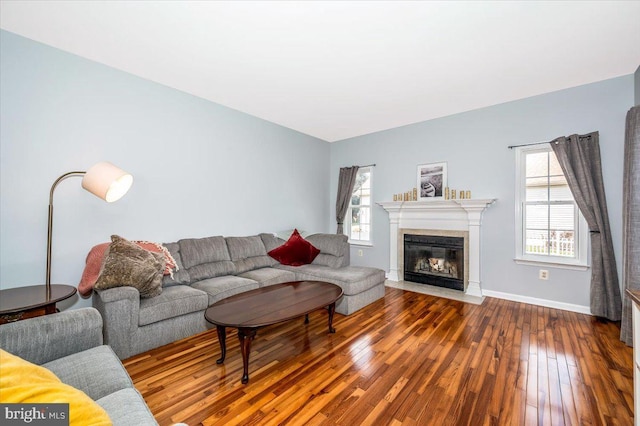 living room featuring a fireplace with flush hearth, wood-type flooring, and baseboards