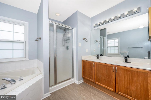 bathroom featuring a sink, double vanity, a shower stall, a garden tub, and wood finished floors
