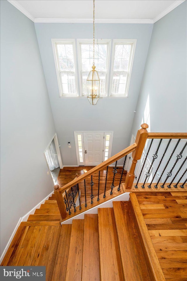 staircase featuring baseboards, a chandelier, crown molding, wood finished floors, and a towering ceiling