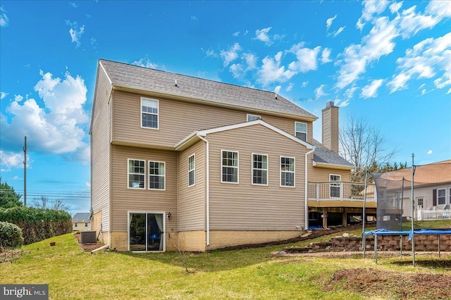 back of property with a trampoline, a deck, a lawn, and a chimney