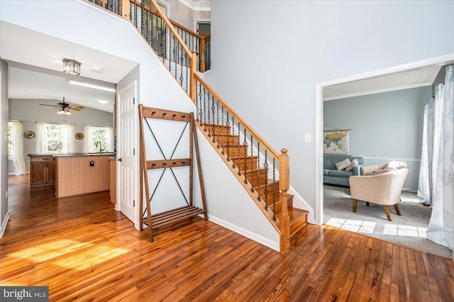 staircase with wood-type flooring, a high ceiling, baseboards, and ceiling fan