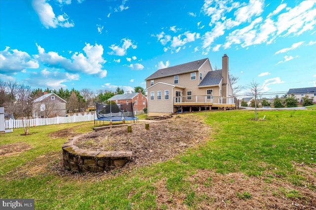 back of house featuring a deck, a trampoline, a lawn, a chimney, and fence