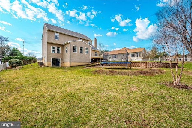 rear view of house featuring fence, a trampoline, and a lawn