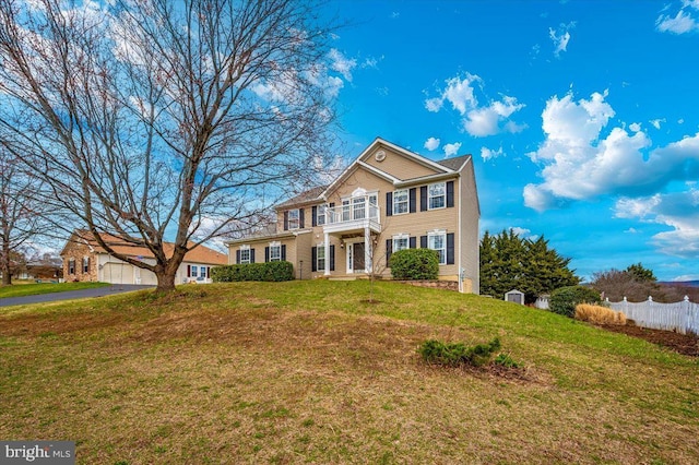 colonial home with a front yard, fence, driveway, and a balcony
