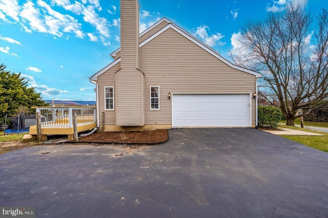 view of property exterior featuring a deck, a trampoline, a garage, a chimney, and driveway