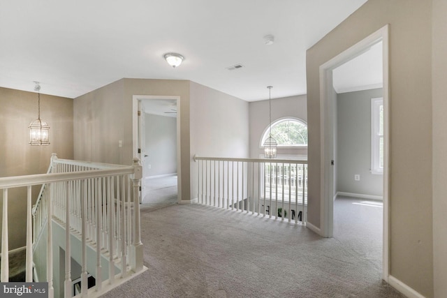 hall with an inviting chandelier, baseboards, carpet flooring, and an upstairs landing