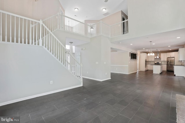 unfurnished living room with a high ceiling, stairs, baseboards, dark tile patterned flooring, and visible vents