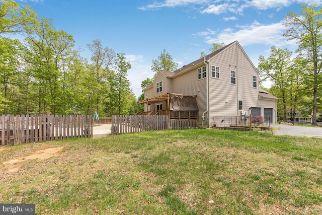 view of home's exterior with driveway, a lawn, a deck, fence, and an attached garage