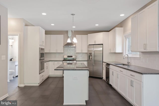 kitchen with wall chimney range hood, appliances with stainless steel finishes, a sink, backsplash, and a kitchen island