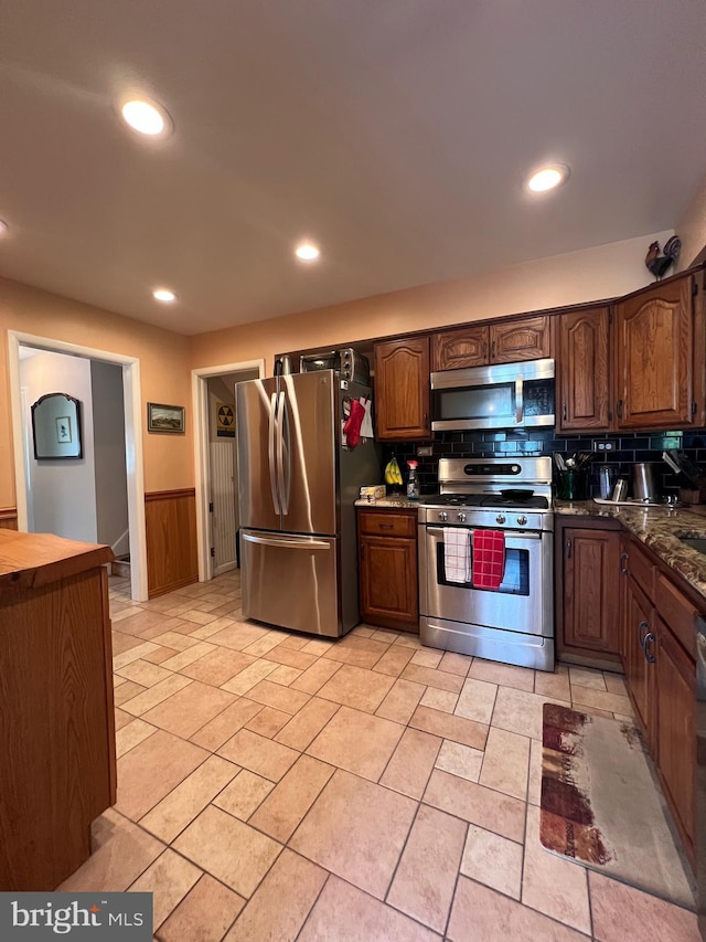 kitchen with dark countertops, appliances with stainless steel finishes, a wainscoted wall, recessed lighting, and tasteful backsplash