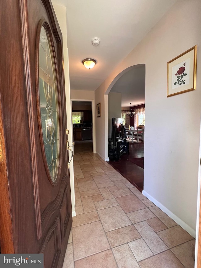hall featuring arched walkways, baseboards, and stone tile flooring