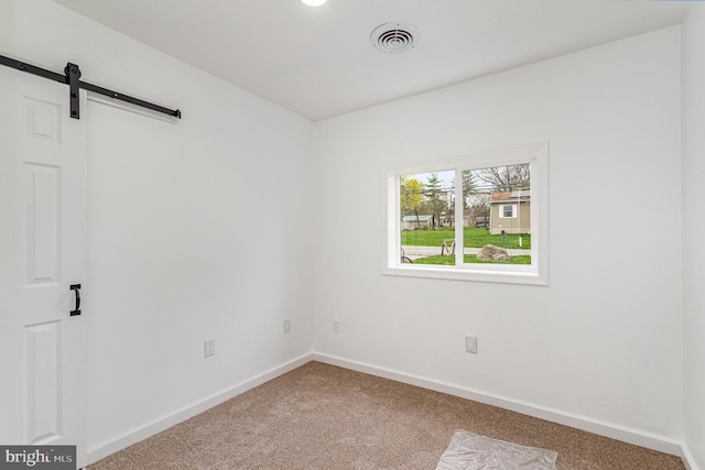 unfurnished room with visible vents, baseboards, carpet, and a barn door