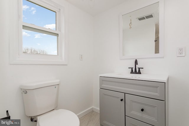 bathroom with vanity, visible vents, toilet, wood finished floors, and baseboards