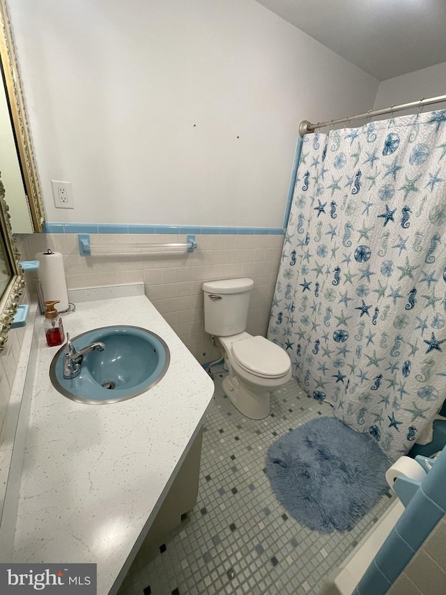 bathroom with vanity, tile patterned flooring, a wainscoted wall, toilet, and tile walls