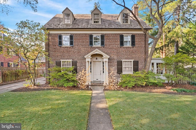 view of front of property featuring fence, brick siding, a chimney, and a front lawn