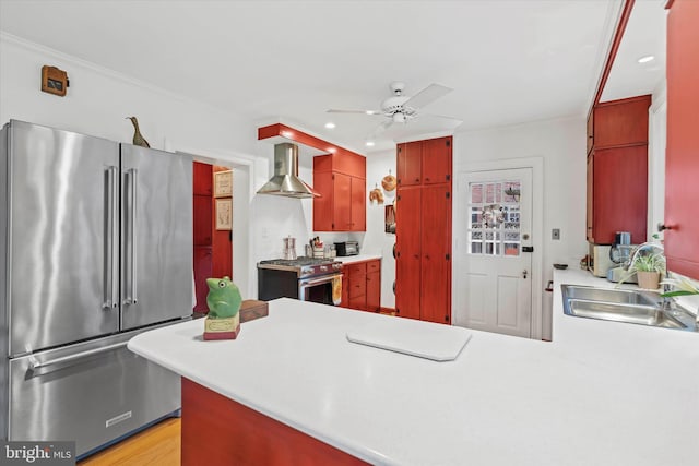 kitchen with premium appliances, a sink, wall chimney range hood, ceiling fan, and a peninsula