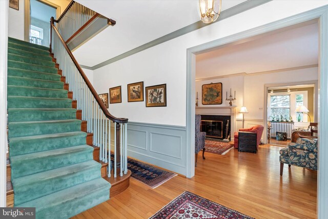 stairs with a decorative wall, radiator heating unit, a glass covered fireplace, wood finished floors, and wainscoting