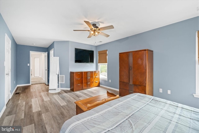 bedroom with light wood-style floors, visible vents, baseboards, and a ceiling fan