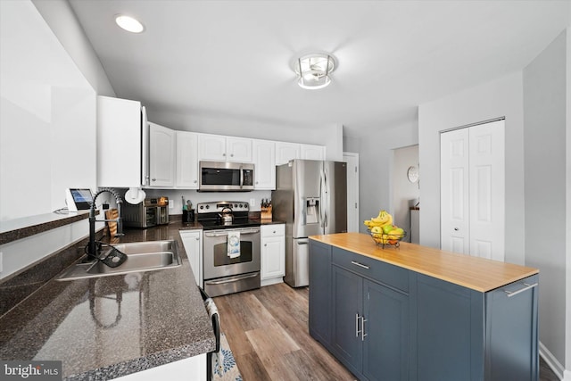 kitchen featuring light wood-type flooring, wood counters, white cabinetry, appliances with stainless steel finishes, and a sink
