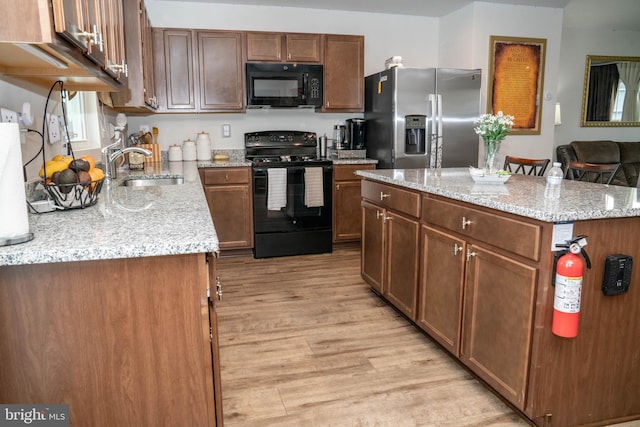 kitchen with light stone counters, black appliances, light wood finished floors, a sink, and a center island