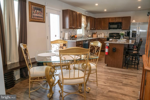 kitchen featuring a sink, light wood-type flooring, black appliances, a breakfast bar, and a kitchen island