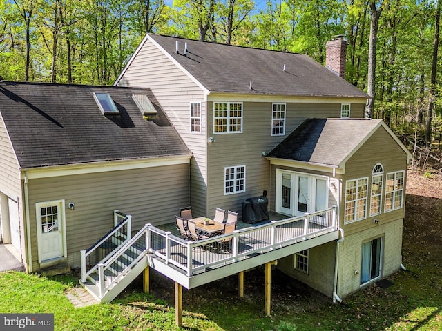 back of property with a garage, a chimney, roof with shingles, and a deck