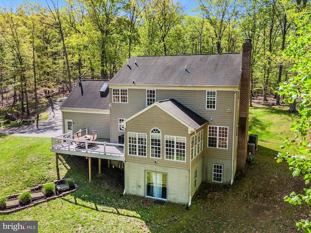 back of property with a shingled roof, a chimney, a yard, and a deck