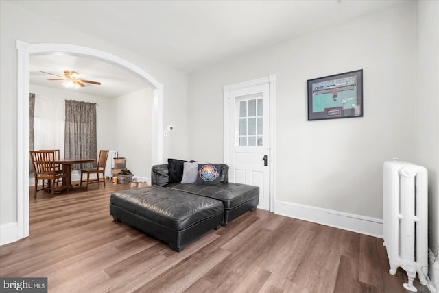 sitting room with arched walkways, ceiling fan, radiator, and wood finished floors