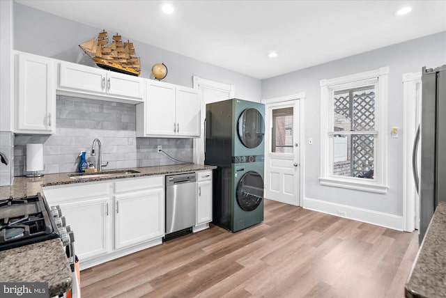 kitchen with a sink, appliances with stainless steel finishes, stacked washer and clothes dryer, and light stone countertops