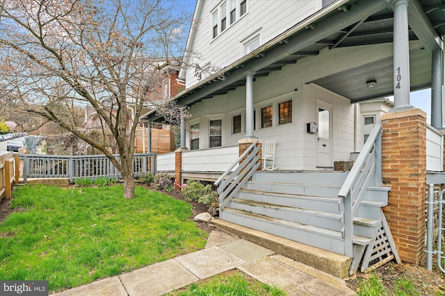 doorway to property featuring a yard, a porch, and fence