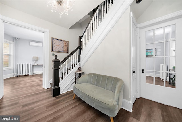 sitting room featuring an inviting chandelier, stairway, radiator heating unit, a wall unit AC, and wood finished floors