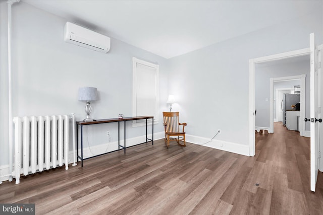 sitting room featuring radiator heating unit, baseboards, wood finished floors, and a wall unit AC