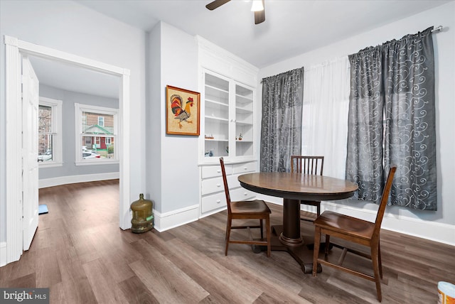 dining area with built in shelves, dark wood-style floors, baseboards, and a ceiling fan