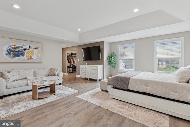 bedroom with a raised ceiling, wood finished floors, baseboards, and recessed lighting