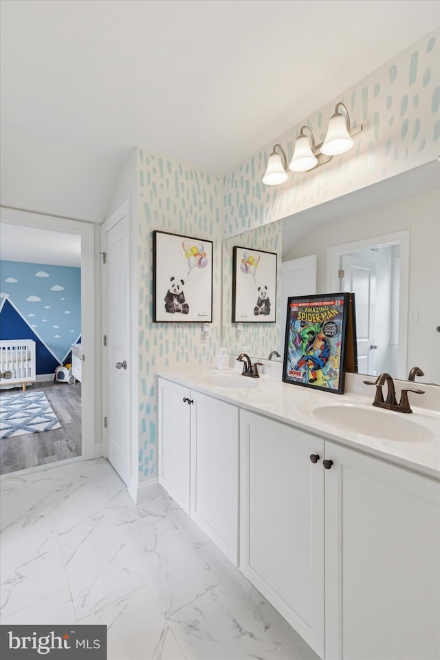 full bathroom featuring baseboards, double vanity, a sink, and wallpapered walls