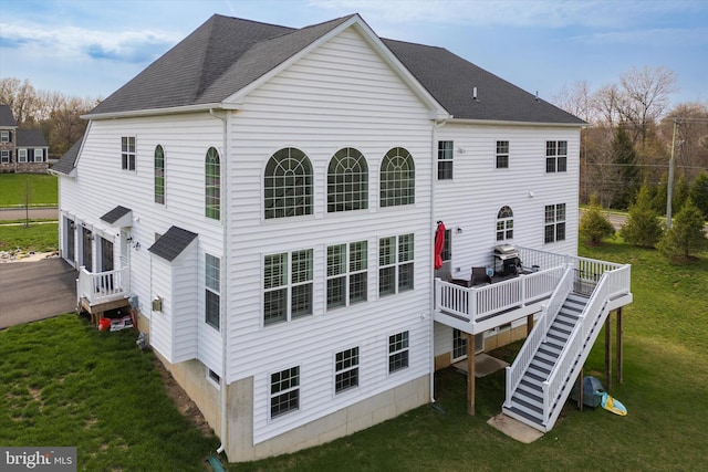 back of property with a yard, stairway, a deck, and a shingled roof
