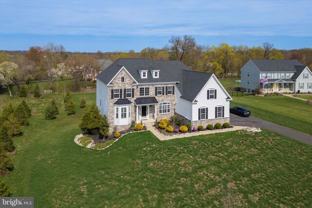 traditional-style house with a front lawn, stone siding, metal roof, and aphalt driveway