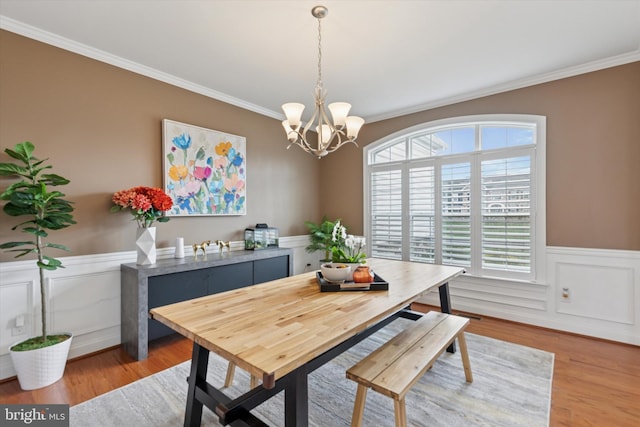 dining space featuring light wood finished floors, a notable chandelier, ornamental molding, and a wainscoted wall
