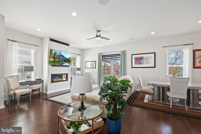 living room featuring ceiling fan, a glass covered fireplace, dark wood-style floors, and baseboards