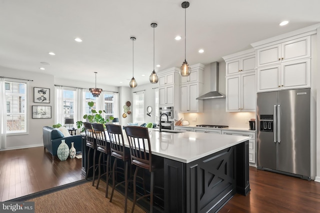 kitchen featuring wall chimney range hood, appliances with stainless steel finishes, dark wood-style floors, and light countertops