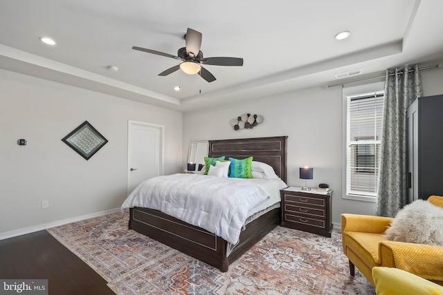 bedroom featuring a ceiling fan, wood finished floors, a raised ceiling, baseboards, and recessed lighting