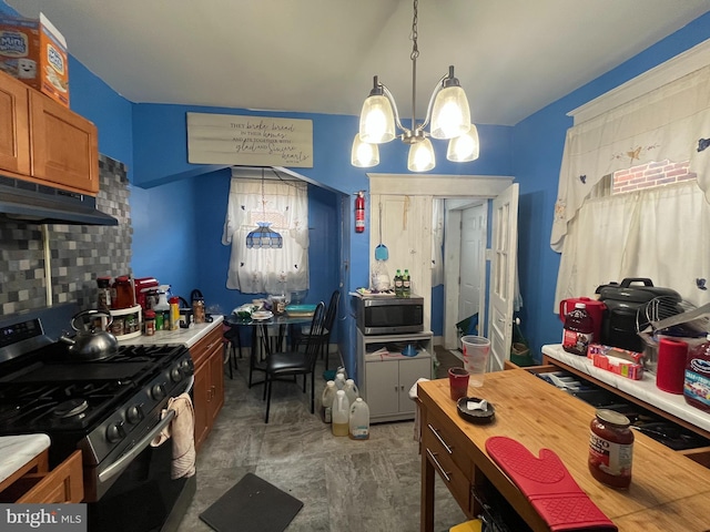 6207 Gardenia St, Philadelphia, PA 19144 - kitchen with tasteful backsplash, a notable chandelier, under cabinet range hood, brown cabinets, and appliances with stainless steel finishes