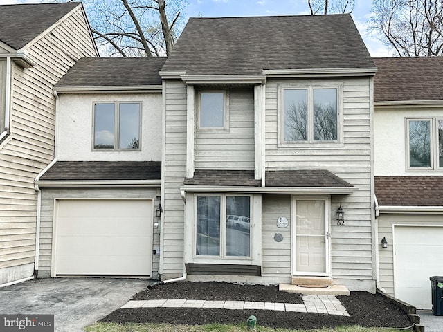 view of property featuring an attached garage, a shingled roof, and driveway