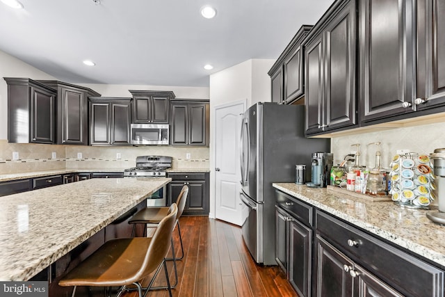 kitchen featuring stainless steel appliances, light stone counters, a breakfast bar, backsplash, and dark wood-type flooring