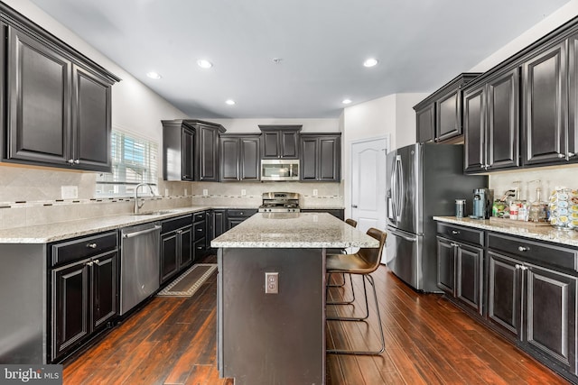 kitchen with a center island, a sink, appliances with stainless steel finishes, dark cabinets, and a breakfast bar area